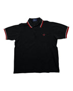 GEGENHALT. Schwarzes Herren-Poloshirt aus Baumwolle mit roten und weißen Kontraststreifen an Kragen und Ärmeln, Fred Perry Logo.